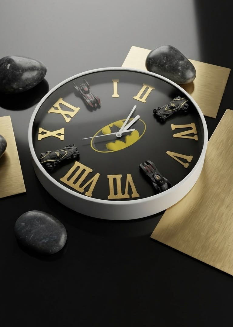 A round wall clock with a black face, gold Roman numerals, and a yellow Batman logo at the center, styled on a dark surface with gold paper and black stones.